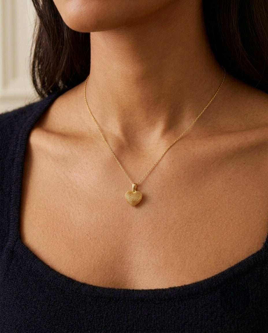 Nahaufnahme einer filigranen Halskette aus 18 Karat Gelbgold mit einem kleinen herzförmigen Anhänger in strukturierter Oberfläche. Der Goldanhänger wird elegant am Dekolleté einer Frau getragen und verleiht dem minimalistischen Schmuckstück eine zeitlose, romantische Ausstrahlung. Hochwertiger Goldschmuck für Damen – ideal als Geschenk oder für den Alltag.