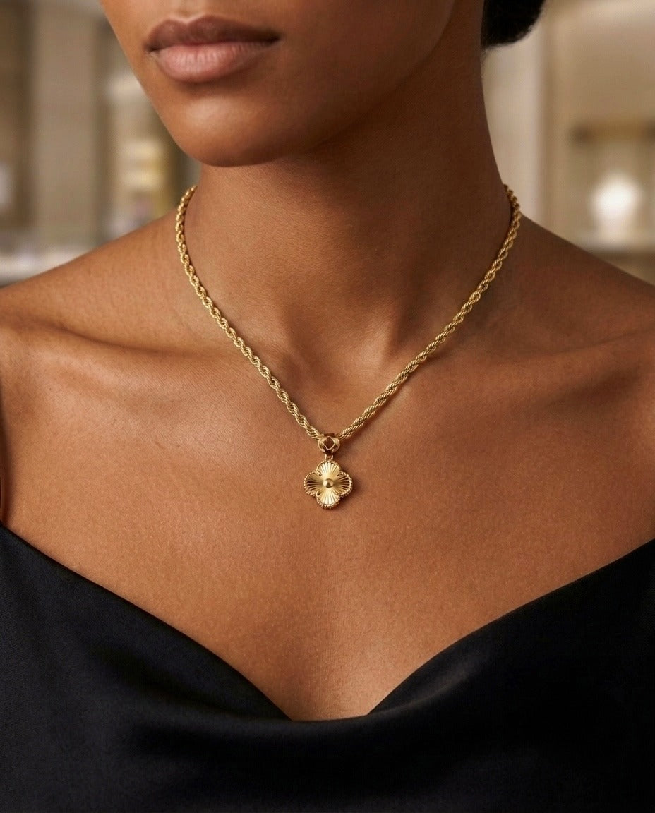 Nahaufnahme einer eleganten 18-Karat-Goldkette mit gedrehter Seilkette und einem filigranen vierblättrigen Kleeblatt-Anhänger. Das Schmuckstück wird auf dem Dekolleté eines Models mit schwarzem schulterfreiem Oberteil getragen und strahlt zeitlose Eleganz sowie feine Handwerkskunst aus.