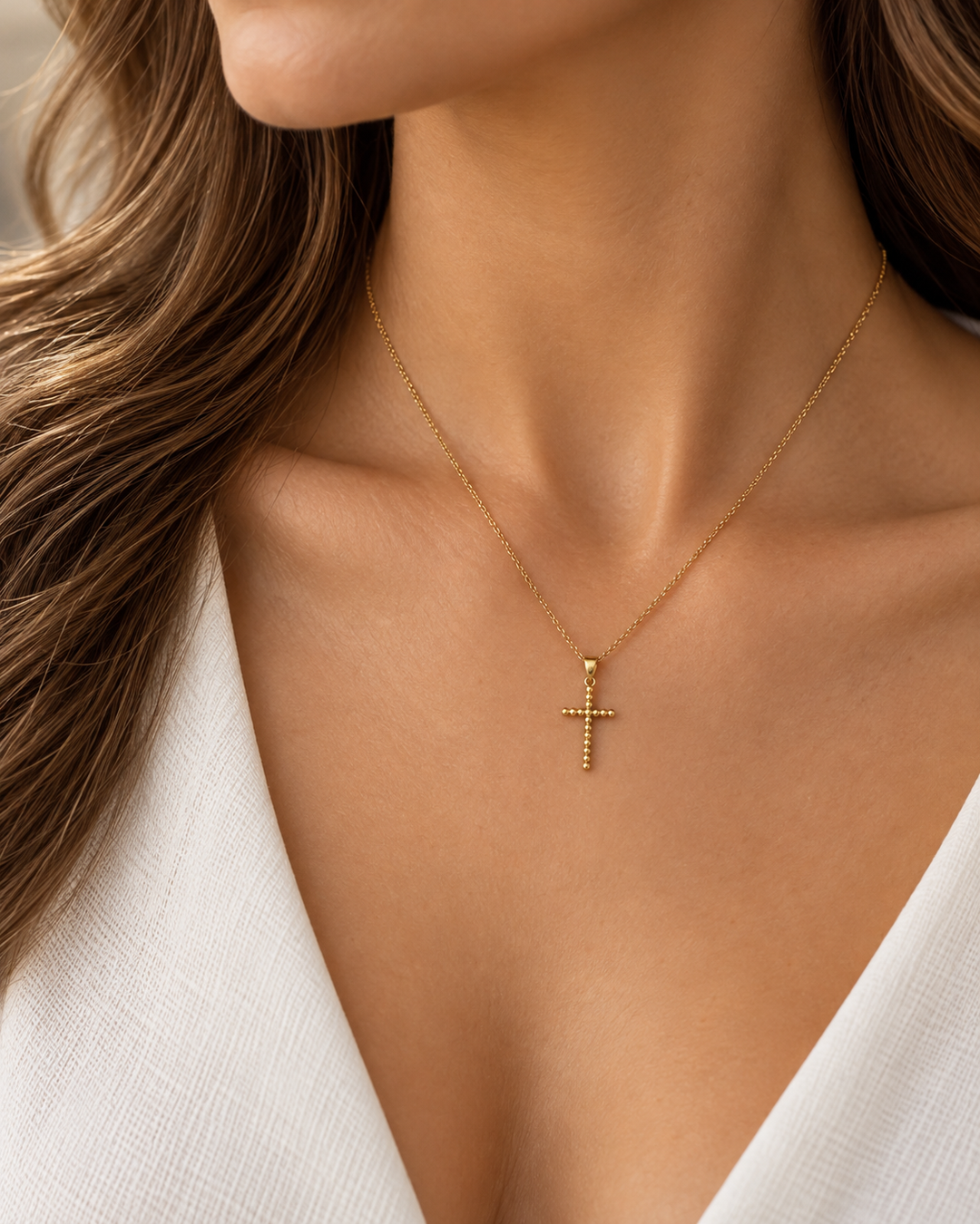 Filigraner Kreuzanhänger aus 18K Gelbgold an einer feinen Goldkette, getragen am Hals einer Frau.