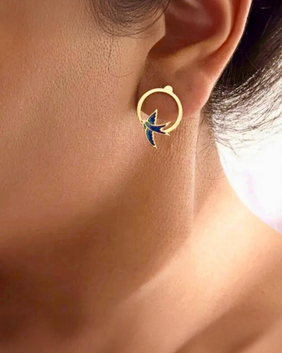 Feine 18k Gold Ohrringe mit Schwalbenmotiv in Blautönen – getragen von einem Model als Symbol für Freiheit & Leichtigkeit.