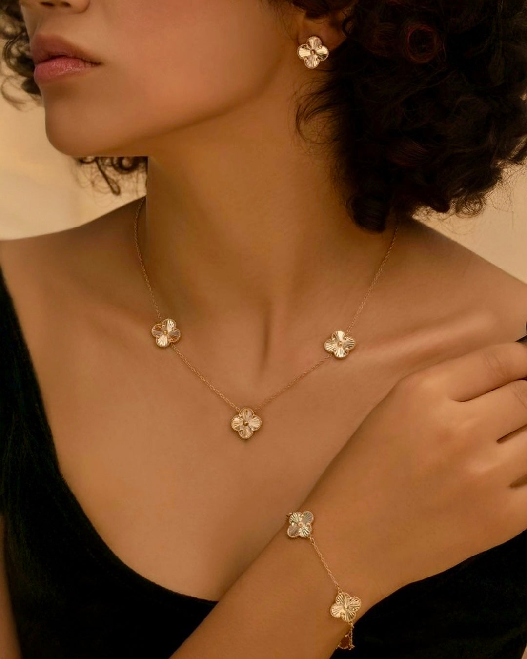 Modell trägt feine Halskette, Ohrringe und Armband aus 18k Gelbgold mit floralen Elementen, elegant inszeniert auf Haut, zeitloser Goldschmuck.