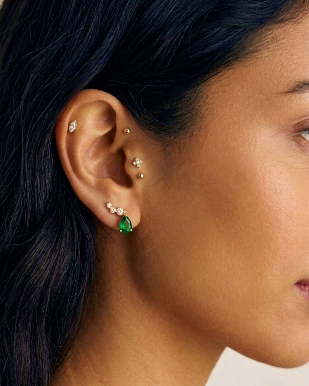 Frau mit dunklem Haar trägt elegante Ohrstecker aus Gelbgold mit tropfenförmigem grünem Stein und funkelnden weissen Akzentsteinen. Die Nahaufnahme zeigt den Schmuck am Ohr in stilvoller, moderner Optik.