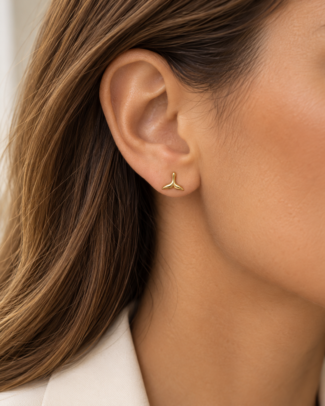 Frau trägt einen zierlichen Walflossen-Ohrstecker aus 18 Karat Gelbgold am Ohr, eleganter minimalistischer Schmuck von Ziba Gold.