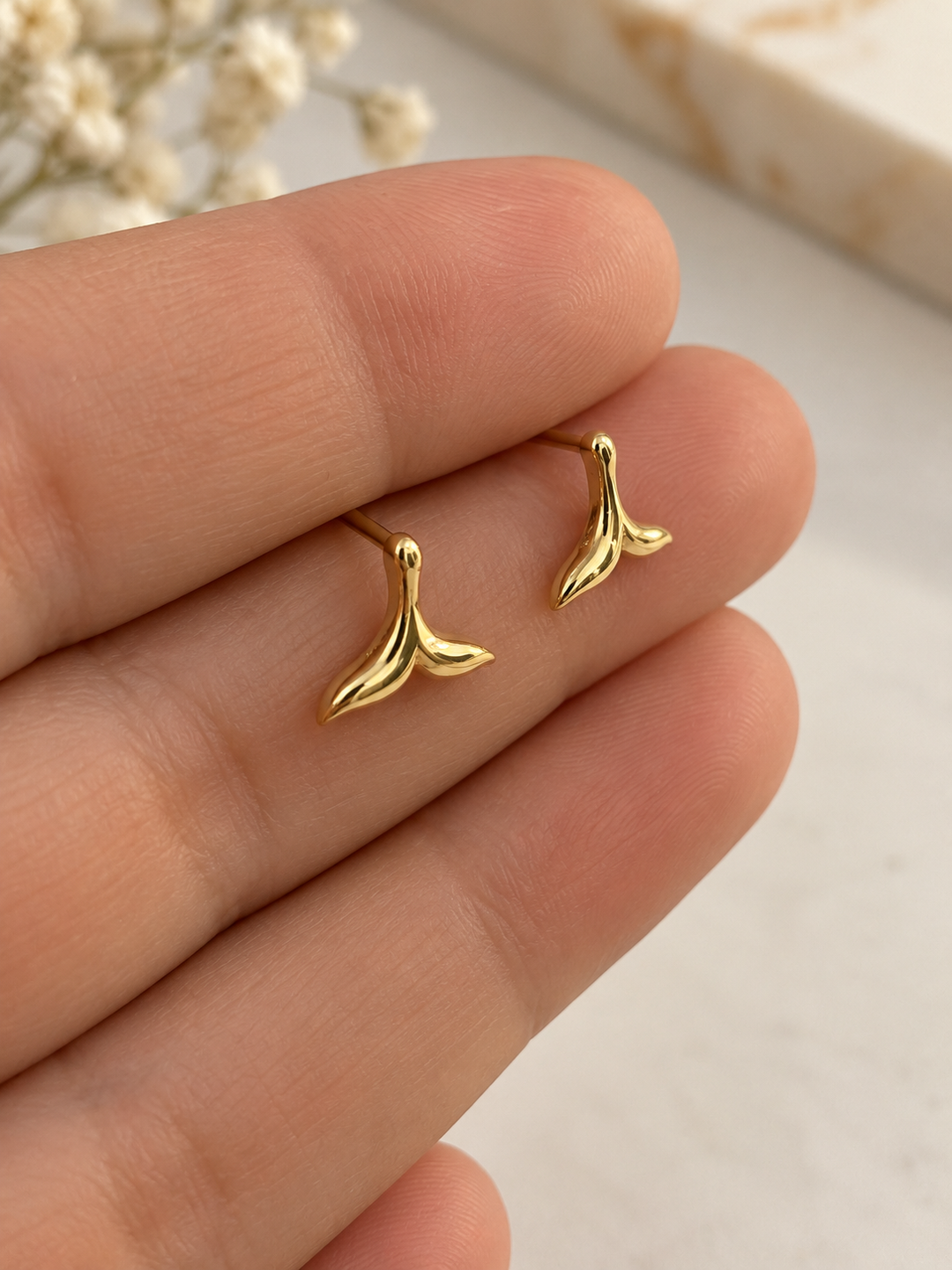 Zwei Ohrstecker aus 18 Karat Gelbgold in geschwungener Walflossenform auf den Fingerspitzen, hochglanzpoliertes Design.