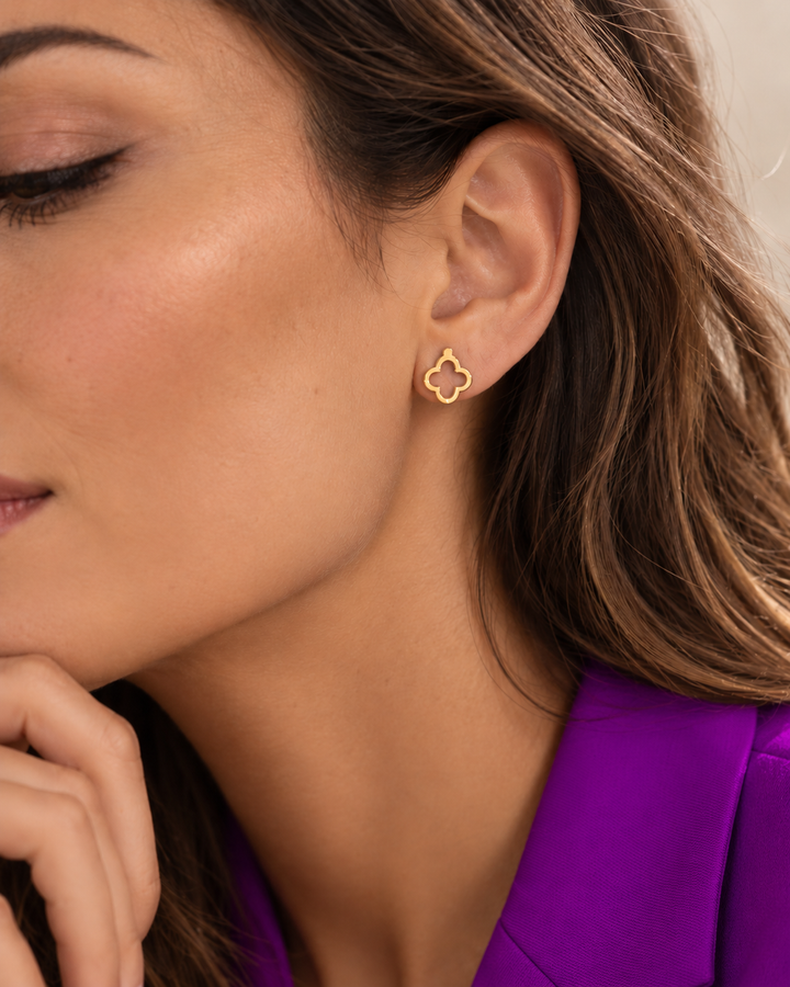 Frau mit filigranem vierblättrigem Ohrstecker aus 18 Karat Gold und kräftig violettem Blazer.