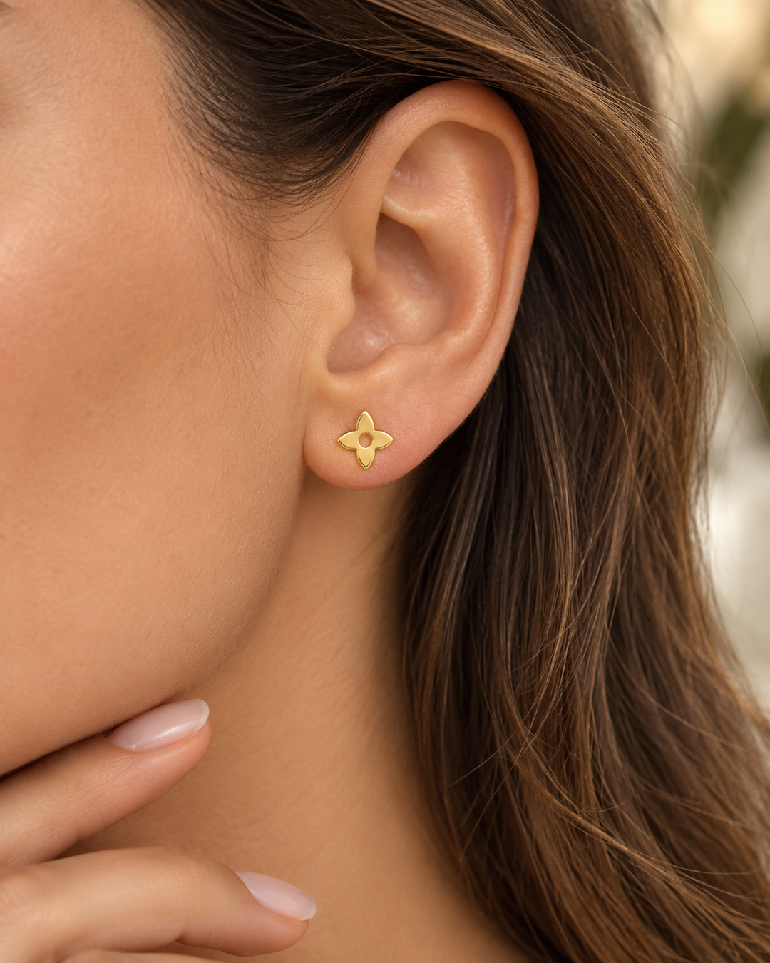 Goldener Ohrstecker in vierblättriger Blütenform mit runder Öffnung, getragen am Ohr einer Frau – Ziba Gold.