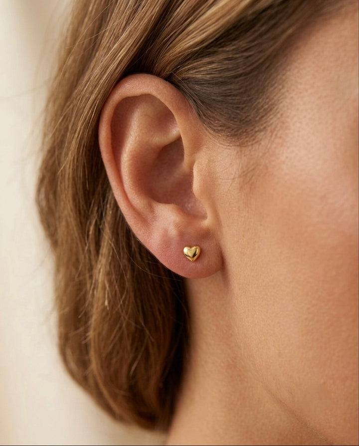 Kleine Herz-Ohrstecker aus 18 Karat Gelbgold in glänzend polierter Ausführung, getragen am Ohr. Die zeitlosen Goldohrstecker in Herzform überzeugen mit ihrem minimalistischen Design und eignen sich ideal für den Alltag sowie als liebevolles Geschenk für Frauen.