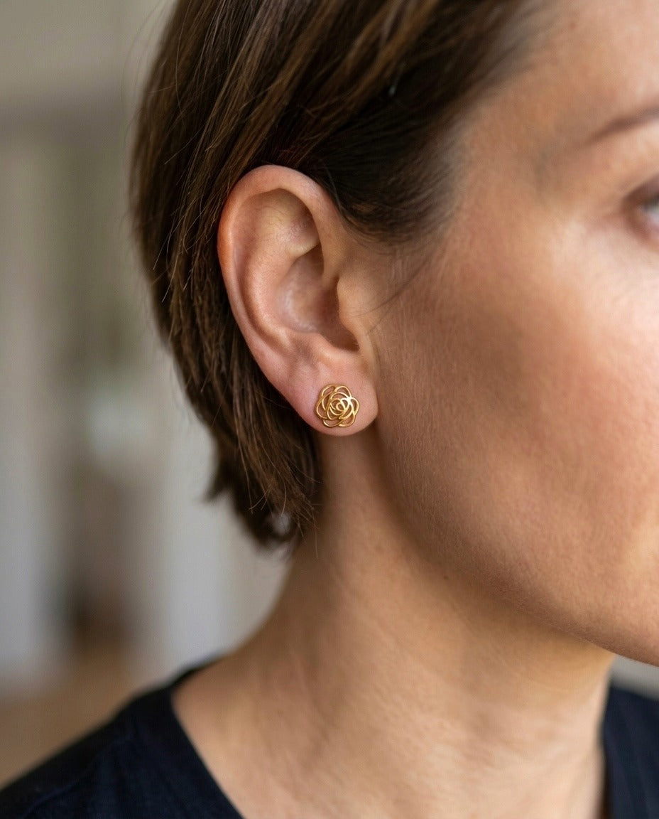 Frau trägt filigrane Ohrstecker aus 18 Karat Gelbgold in Form einer stilisierten Blüte mit ineinander verschlungenen Linien. Die eleganten Gold-Ohrstecker sitzen dezent am Ohr und verleihen jedem Outfit eine zeitlose, feminine Ausstrahlung. Handgefertigter Goldschmuck für Alltag und besondere Anlässe.
