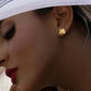 Nahaufnahme einer Person im Profil mit einem weißen Kopftuch. Am Ohr wird ein kleiner, glänzender Ohrstecker aus Gelbgold in Form eines vierblättrigen Kleeblatts getragen. Das Schmuckstück wirkt schlicht, elegant und modern. Der Fokus liegt auf dem Ohrschmuck, während Gesicht und Hintergrund weich und dezent dargestellt sind.