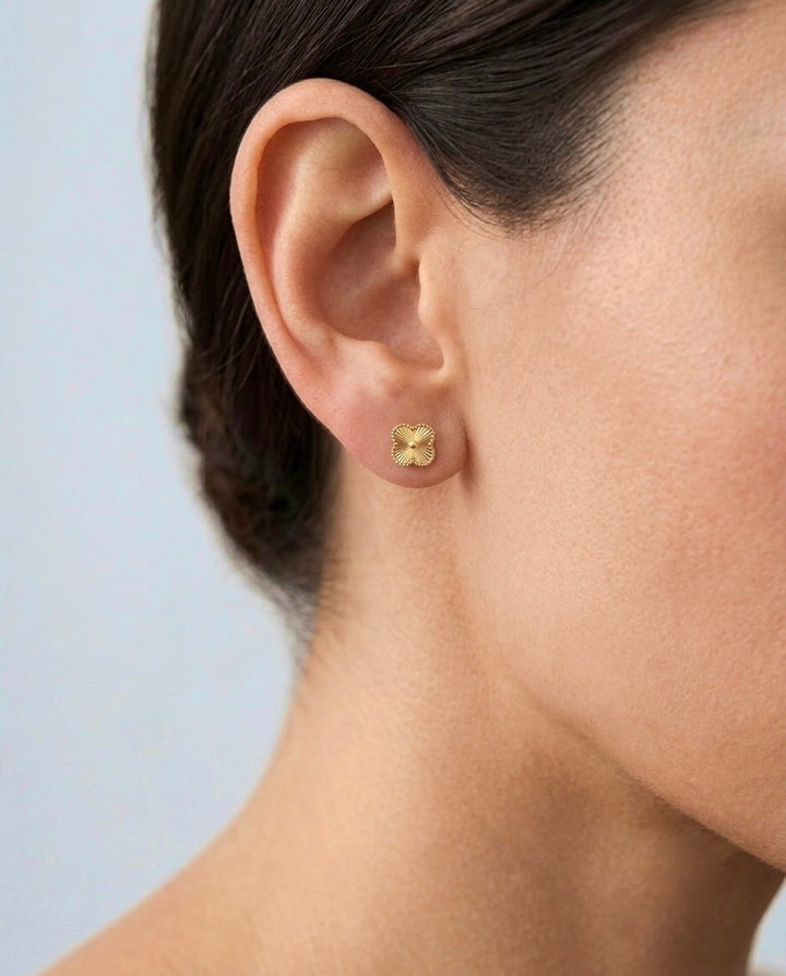 18 Karat Gelbgold-Ohrstecker in filigraner Kleeblattform, getragen am Ohr. Die feine Strahlenstruktur und der dekorative Kugelrand verleihen den eleganten Steckohrringen einen dezenten Glanz und machen sie zu einem zeitlosen Begleiter für Alltag und besondere Anlässe.