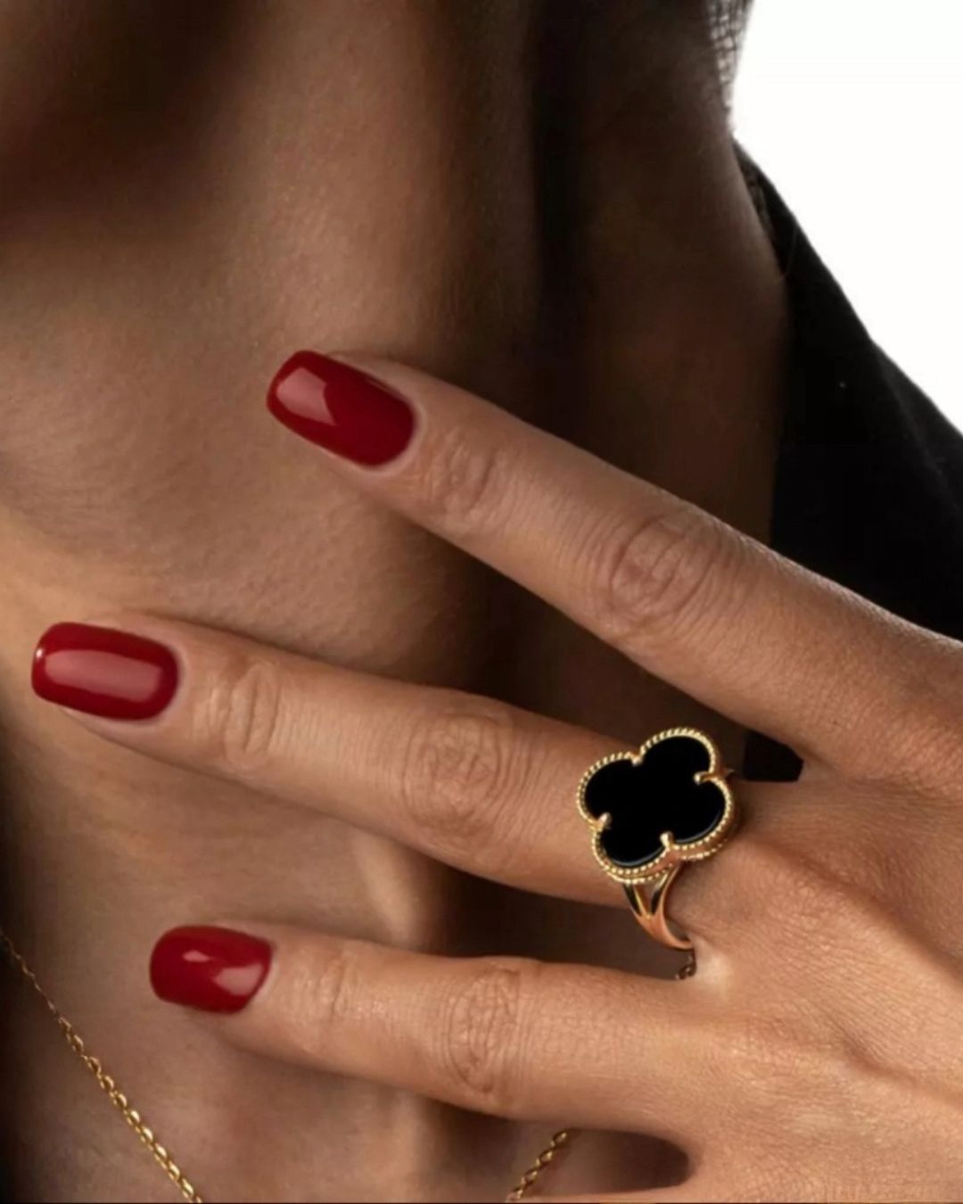 Goldring mit schwarzem Onyx-Kleeblatt auf Hand getragen – mit rotem Nagellack