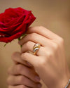 Hand mit dreifarbigem Ring aus Gelbgold, Weissgold hält eine rote Rose – eleganter Schmuck in Nahaufnahme