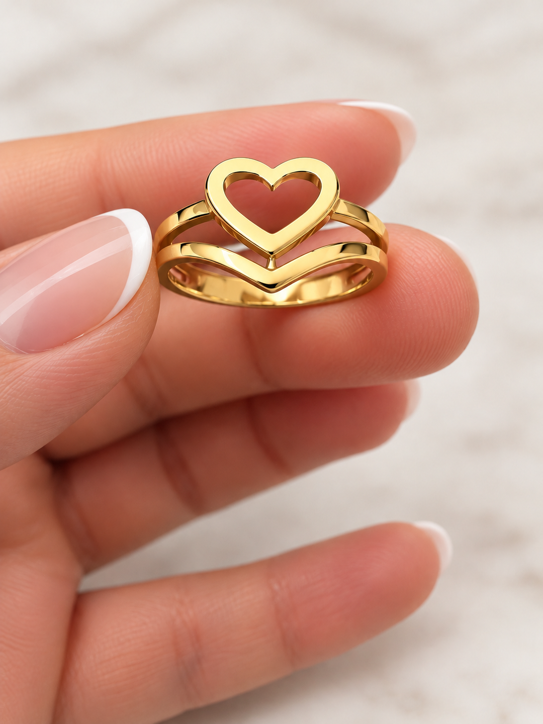 Ring Peyvand aus 18K Gelbgold mit offenem Herzmotiv und doppelt geschwungener Ringschiene, Nahaufnahme zwischen den Fingern.