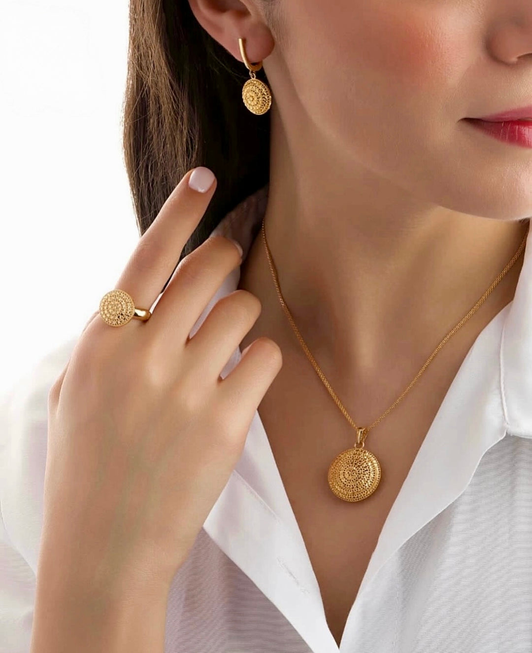 Nahaufnahme einer Frau mit weißem Hemd, die einen 18k Gelbgold-Ring mit rundem, filigran durchbrochenem Sonnenscheiben-Design trägt, passend zu Ohrringen und Halskette im gleichen Stil.