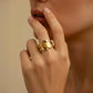 Elegante Nahaufnahme einer Frau mit modernem Statement-Ring in Goldoptik. Das skulpturale Design mit geschwungenen Linien und glänzenden Akzenten verleiht dem Schmuckstück eine luxuriöse, kunstvolle Ausstrahlung und setzt einen stilvollen Fokus auf die Hand.