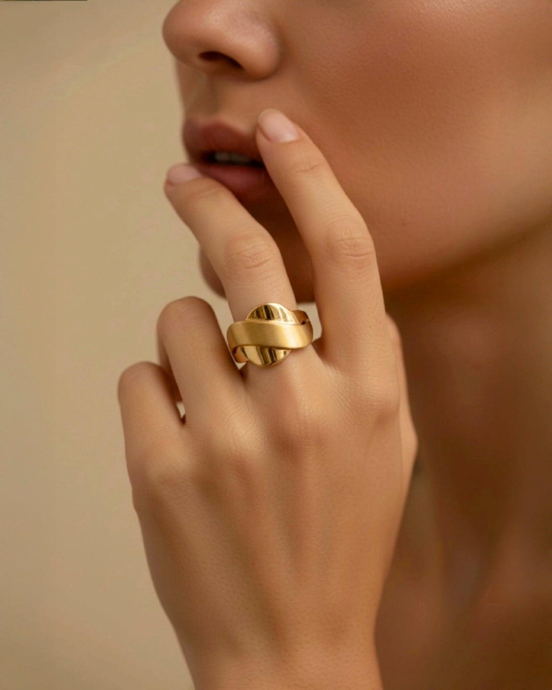 Elegante Nahaufnahme einer Frau mit modernem Statement-Ring in Goldoptik. Das skulpturale Design mit geschwungenen Linien und glänzenden Akzenten verleiht dem Schmuckstück eine luxuriöse, kunstvolle Ausstrahlung und setzt einen stilvollen Fokus auf die Hand.