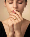 Frau mit geschlossenen Augen trägt einen breiten, hochglanzpolierten 18k Gelbgold-Ring mit Kettenstruktur am Finger – eleganter Goldschmuck in zeitloser, minimalistischer Ästhetik.