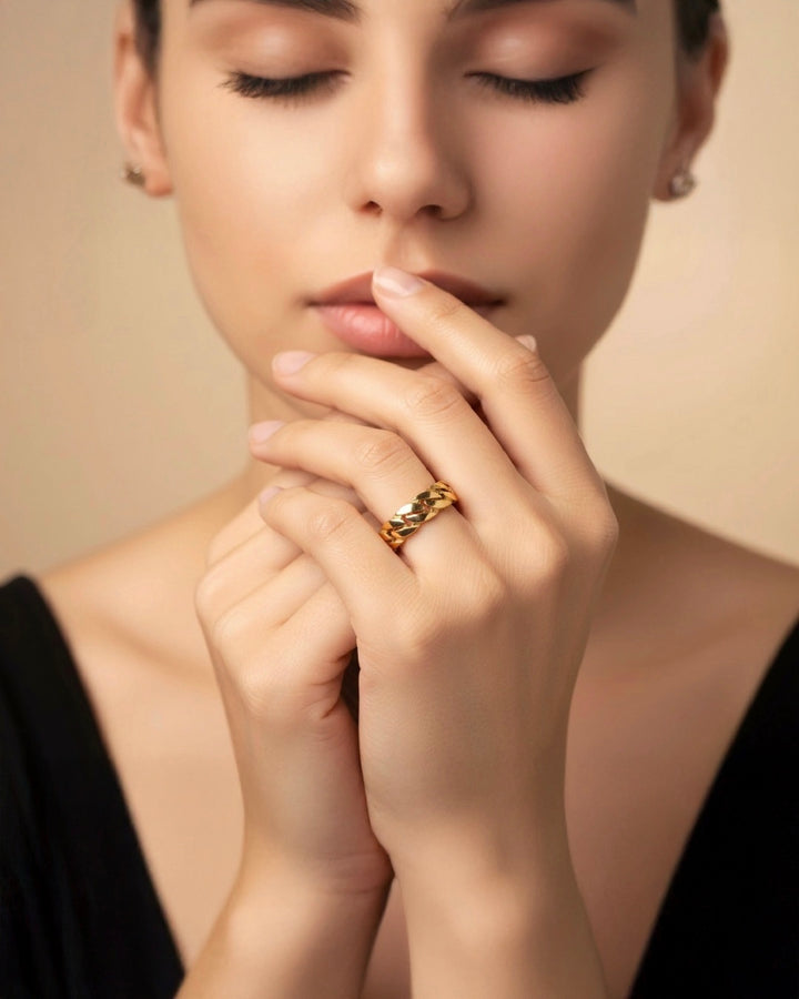 Frau mit geschlossenen Augen trägt einen breiten, hochglanzpolierten 18k Gelbgold-Ring mit Kettenstruktur am Finger – eleganter Goldschmuck in zeitloser, minimalistischer Ästhetik.