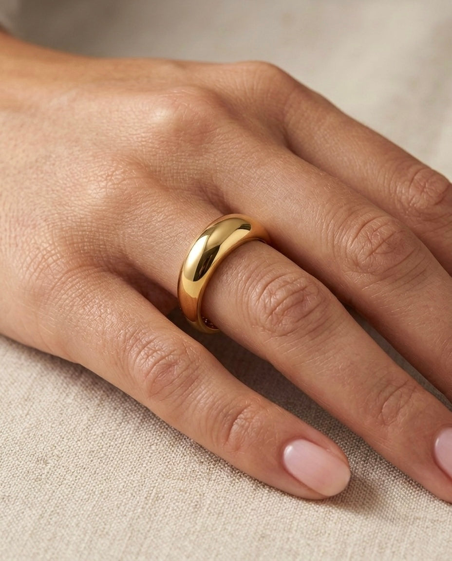 18k Gelbgold Ring mit breiter, abgerundeter Form und glänzend polierter Oberfläche, getragen an einer Hand auf hellem Stoff.