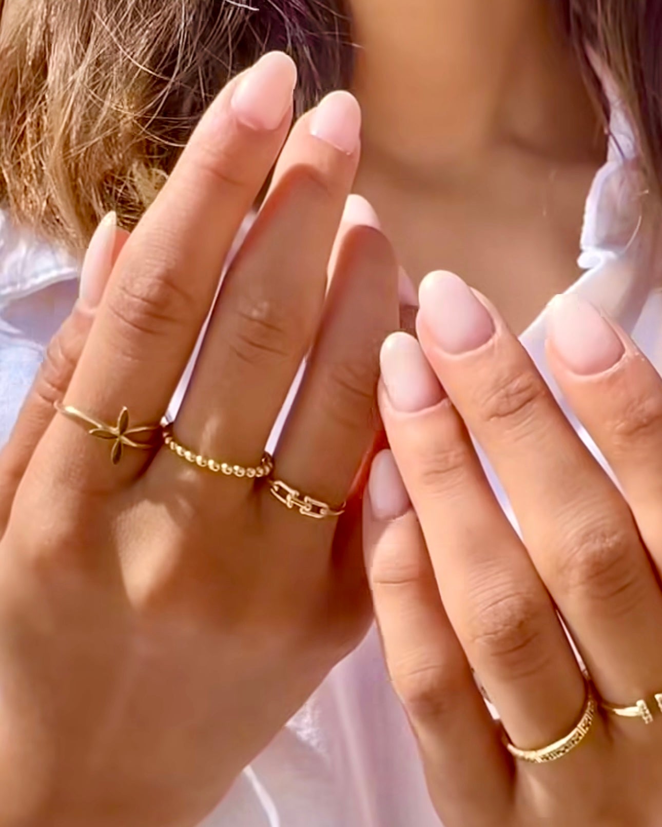 Nahaufnahme zweier Hände mit mehreren Ringen aus 18 Karat Gelbgold – darunter ein zarter Ring mit Blütenmotiv, ein Kügelchen-Ring, ein feiner Gliederring sowie minimalistische Bandringe. Elegant kombiniert für einen modernen und femininen Look.