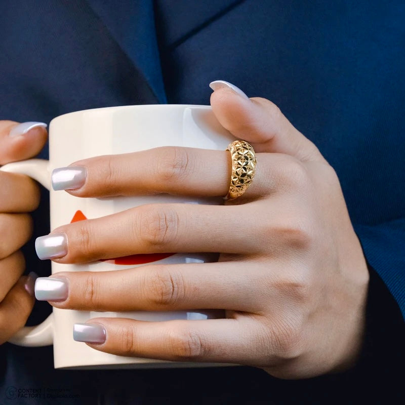 Hand hält eine Tasse, geschmückt mit dem Ring „Golbarg-e Pichideh“ aus 18 Karat Gelbgold – detailreich verflochtenes Blütenmuster, kunstvoll gearbeitet und elegant im Alltag tragbar.