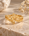 Filigraner Ring aus 18 Karat Gelbgold mit kunstvoller, durchbrochener Struktur und facettierten Details, stilvoll auf hellem Naturstein in warmem Licht inszeniert.