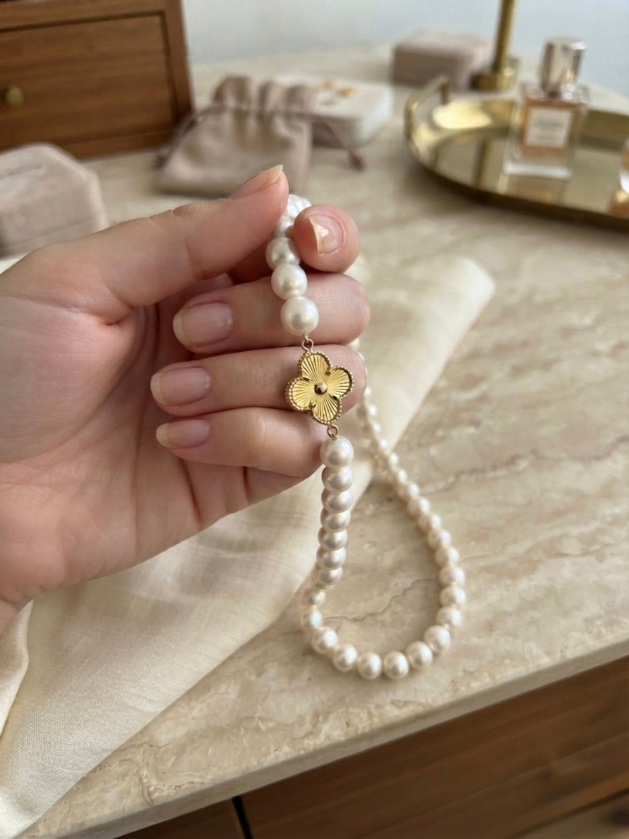 Perlenkette mit dekorativem Blumenanhänger aus 18 Karat Gelbgold, elegant in der Hand präsentiert – edler Perlenschmuck von ZIBA GOLD.