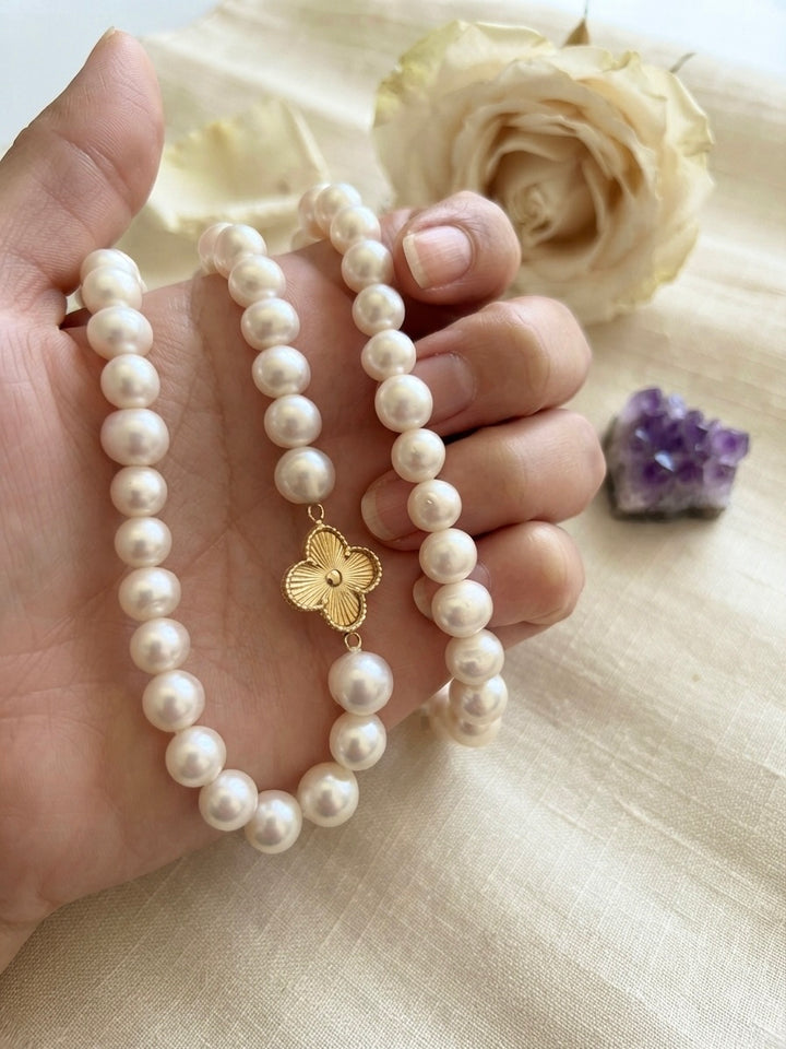 Perlenkette mit weissen Perlen und floralem Schmuckelement aus 18 Karat Gelbgold, in der Hand präsentiert – elegante Perlenkette von ZIBA GOLD.