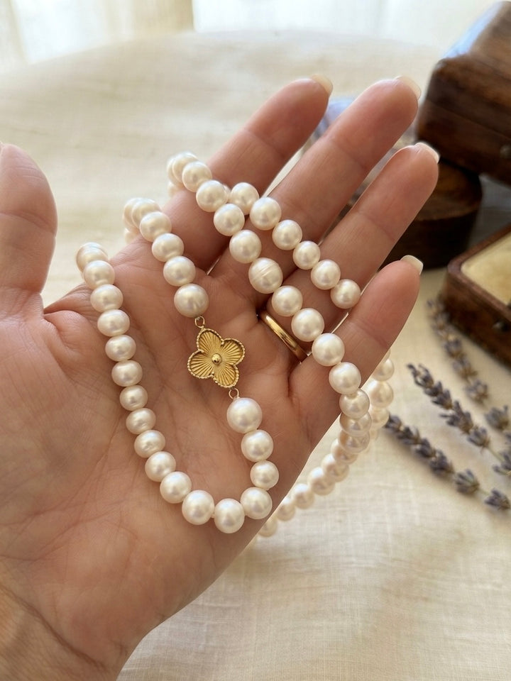 Perlenkette mit weissen Perlen und floralem Schmuckelement aus 18 Karat Gelbgold, elegant auf einer Hand präsentiert – edler Perlenschmuck von ZIBA GOLD.