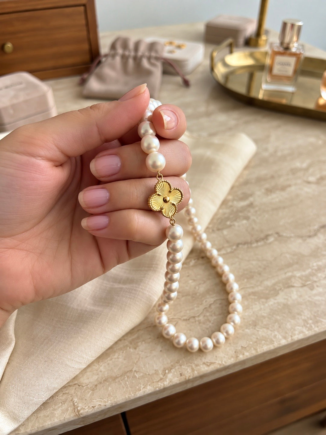 Perlenkette mit dekorativem Blumenanhänger aus 18 Karat Gelbgold, elegant in der Hand präsentiert – edler Perlenschmuck von ZIBA GOLD.