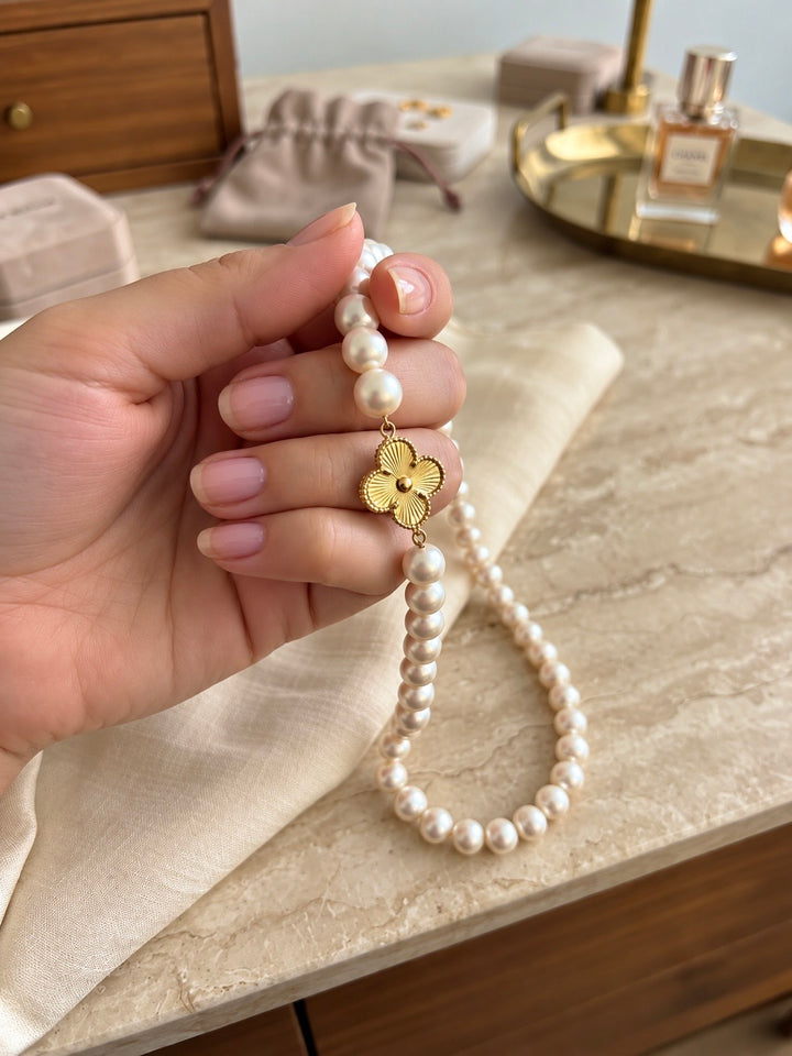Perlenkette mit dekorativem Blumenanhänger aus 18 Karat Gelbgold, elegant in der Hand präsentiert – edler Perlenschmuck von ZIBA GOLD.