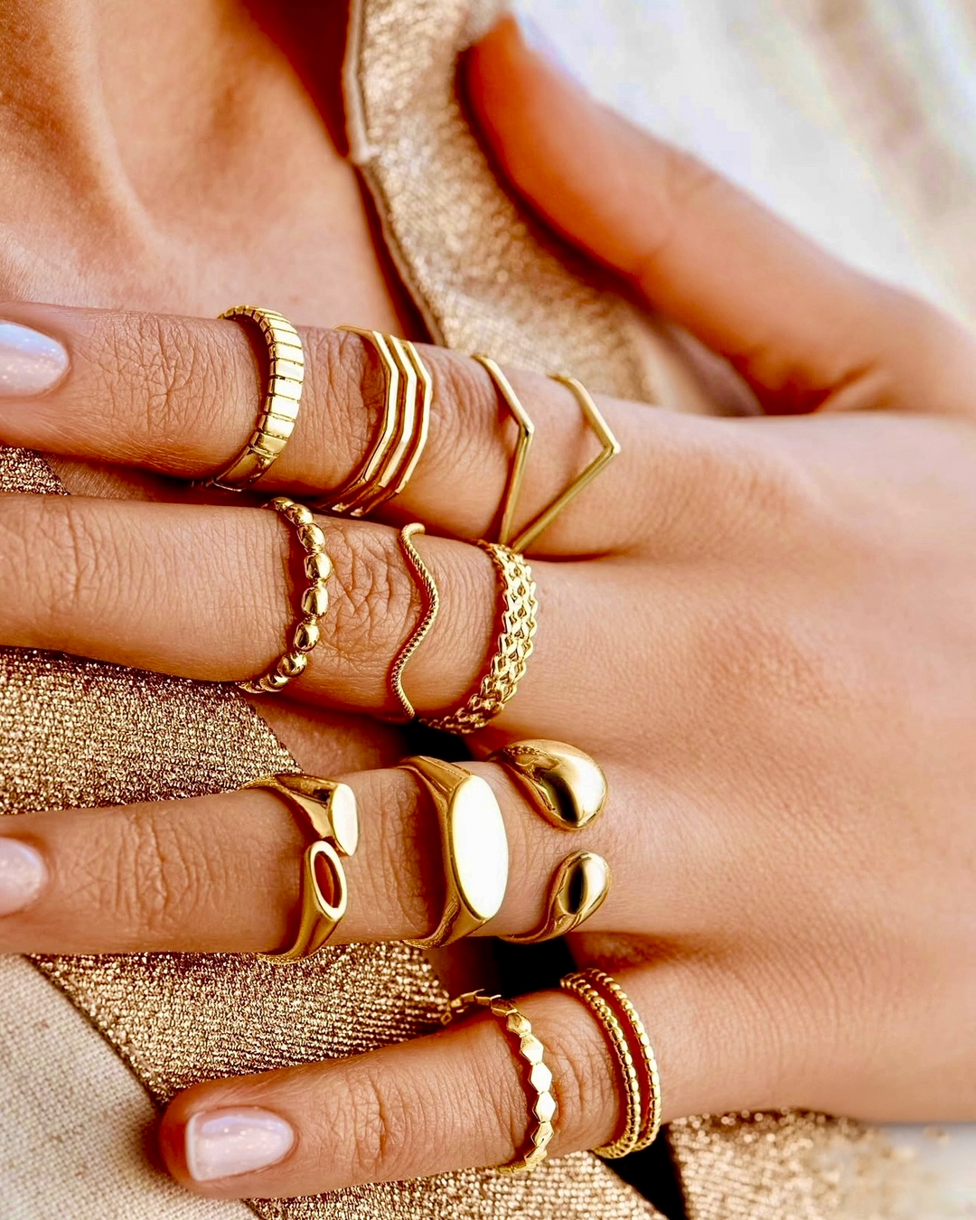 Mehrere elegante Ringe aus 18 Karat Gelbgold an einer Hand getragen – verschiedene Designs von filigran bis massiv, darunter geometrische Formen, glatte Oberflächen und feine Kettenstrukturen, kombiniert zu einem modernen und luxuriösen Look.