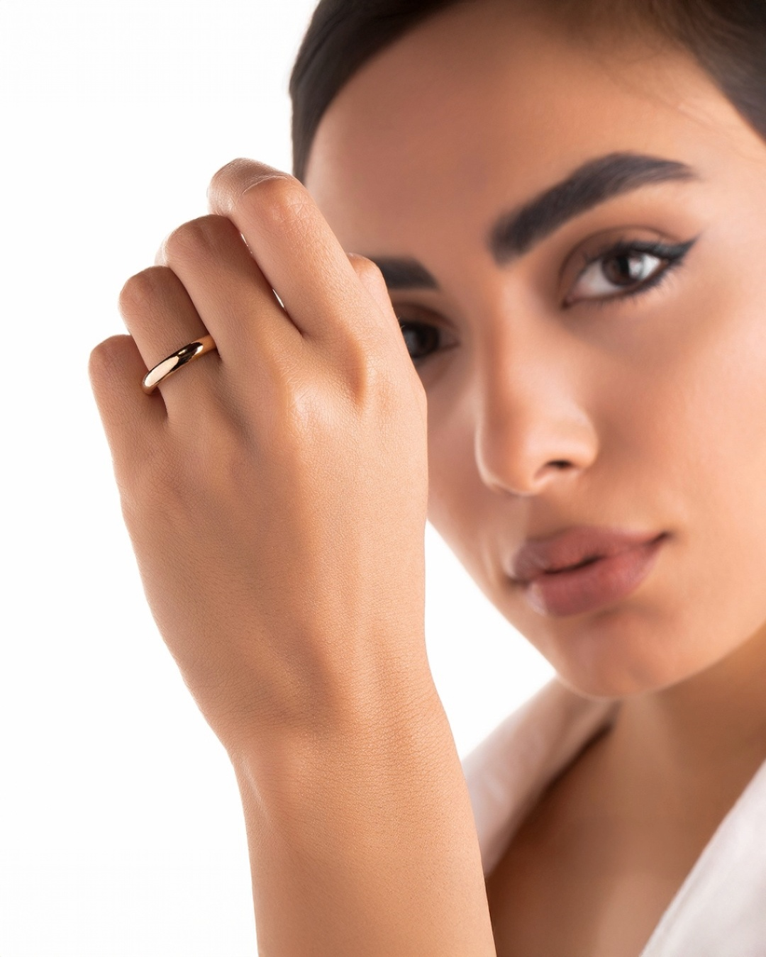 Nahaufnahme einer Frau mit elegantem 18k Goldring an der Hand, dezentes Make-up und weißes Outfit, stilvolles Schmuck-Foto mit Fokus auf den Ring.
