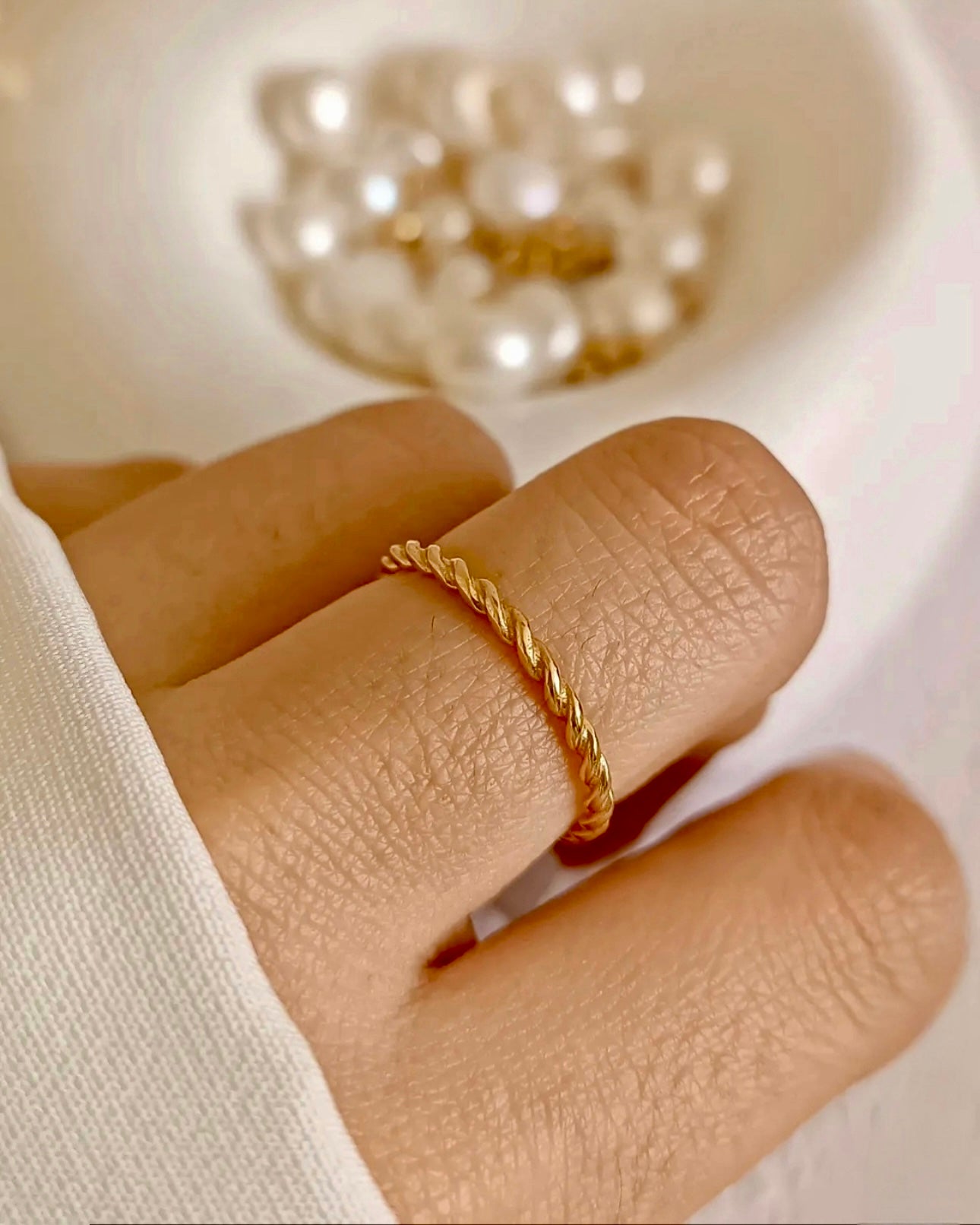 Zarter 18k Gelbgold-Twistring an einer Hand, feine gedrehte Struktur, elegante Nahaufnahme hochwertigen Goldschmucks.