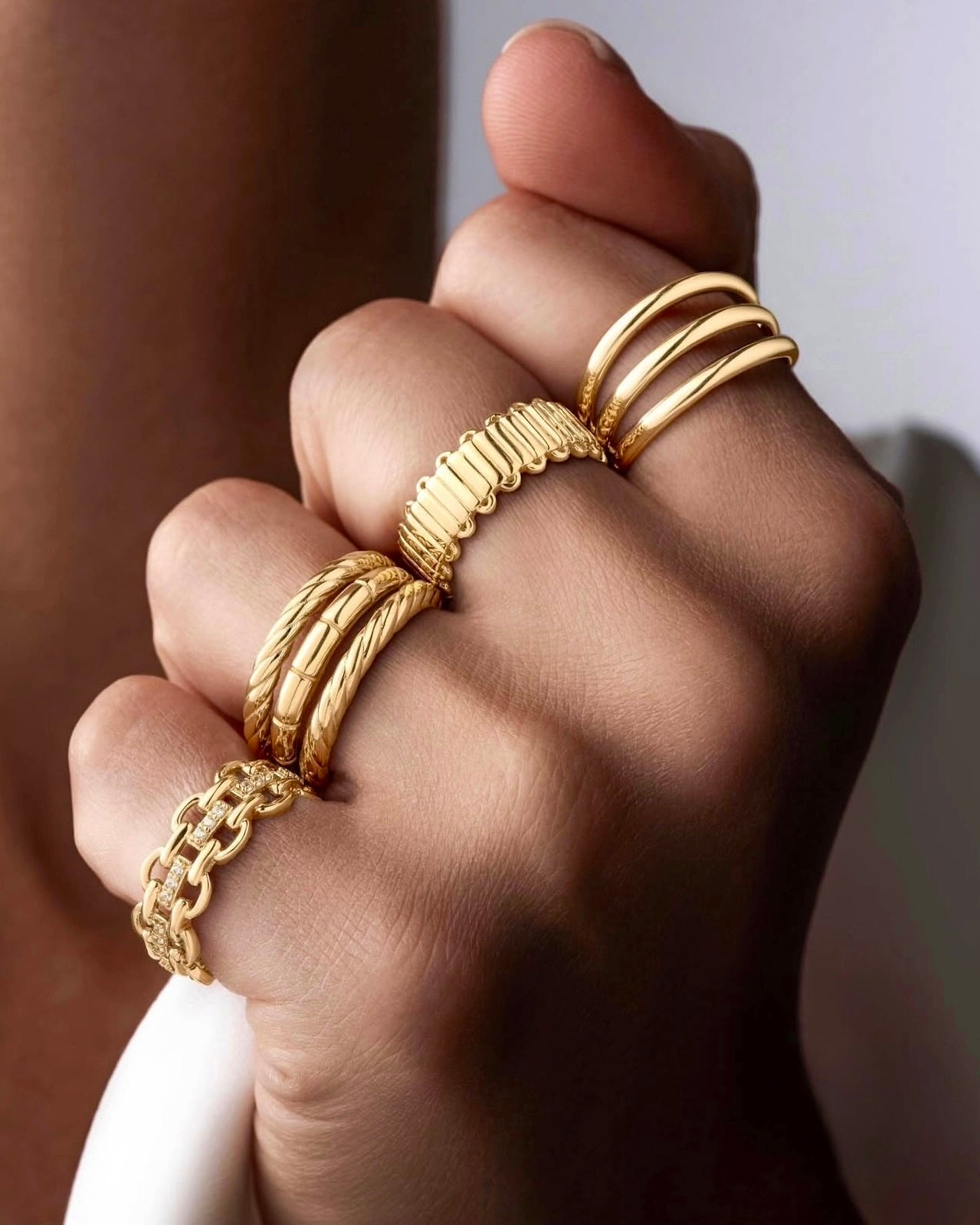 Hand mit mehreren 18k Goldringen, darunter gedrehter Ring ‚Reshhe-ye Talâ‘ – Schmuckstyling Nahaufnahme