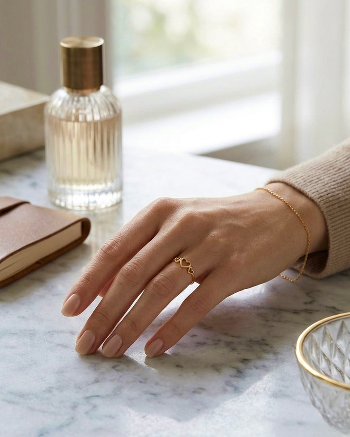 18k Gelbgold Ring mit filigranem Herzdesign an einer Hand, kombiniert mit feinem Goldarmband auf hellem Marmor.