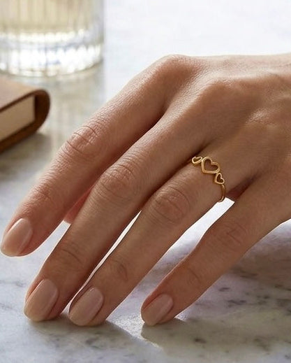 18k Gelbgold Ring mit filigranem Herzdesign an einer Hand, kombiniert mit feinem Goldarmband auf hellem Marmor.