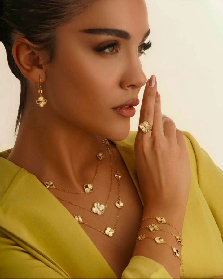 Elegantes Model in grünem Kleid trägt fein abgestimmten 18k-Gelbgoldschmuck: mehrreihige Halsketten mit kleeblattförmigen Anhängern, passende Ohrringe, Armband und Ring – stilvoll, feminin und harmonisch inszeniert.