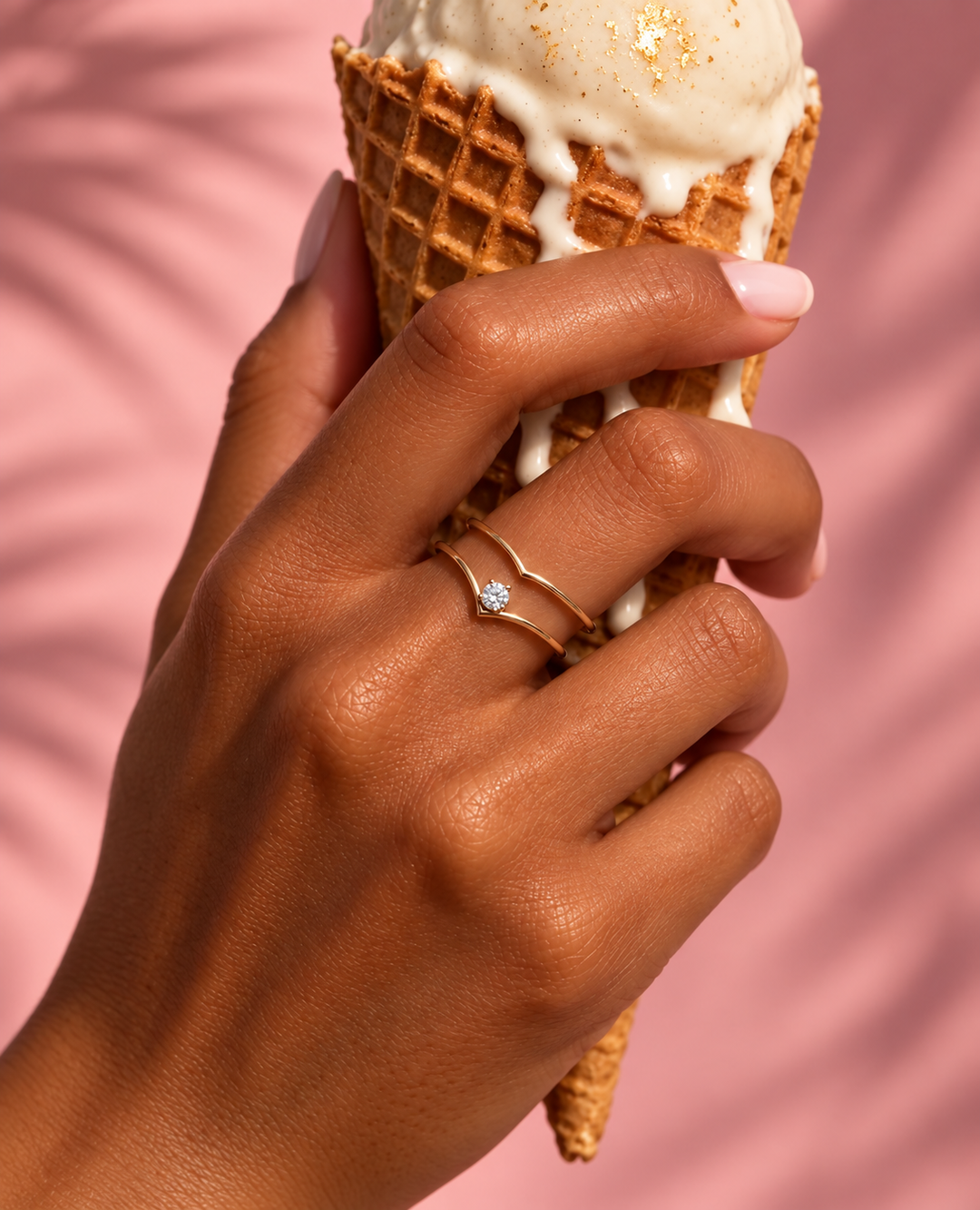 Taj Ring aus 18k Gelbgold mit einzelnem Zirkonia getragen an der Hand vor rosafarbenem Hintergrund