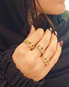 Hand einer Frau mit dunkel lackierten Nägeln, geschmückt mit drei Ringen aus 18 Karat Gelbgold im markanten Kettenglieder-Design. Moderner, auffälliger Statement-Look, kombiniert mit schwarzer Kleidung.